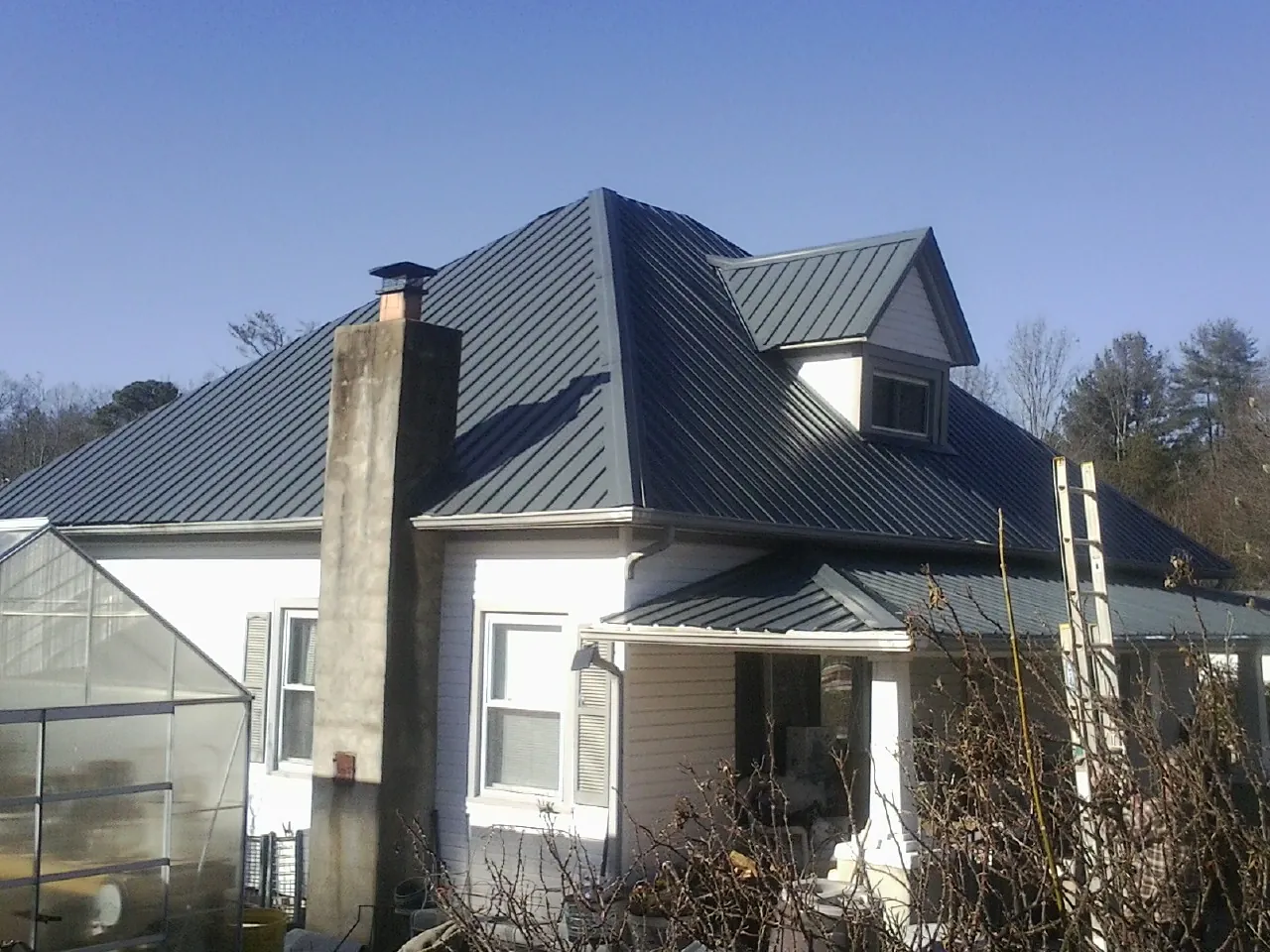 Dark blue standing seam metal roof on a white farmhouse with dormer — Slate & Tile Roof Repair by Roofing Brothers in Kings Mountain