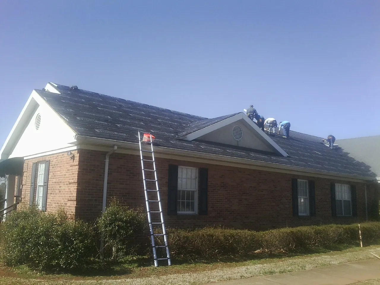 Crew tearing shingles off a brick ranch roof with a ladder set — Emergency Roof Repair work by our crew in Kings Mountain