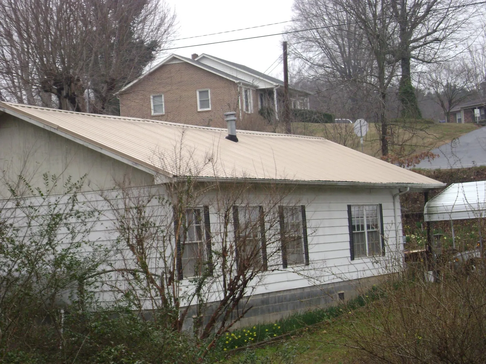 Tan metal roof on a white sided house set into a hillside — Commercial Roofing by Roofing Brothers in Kings Mountain