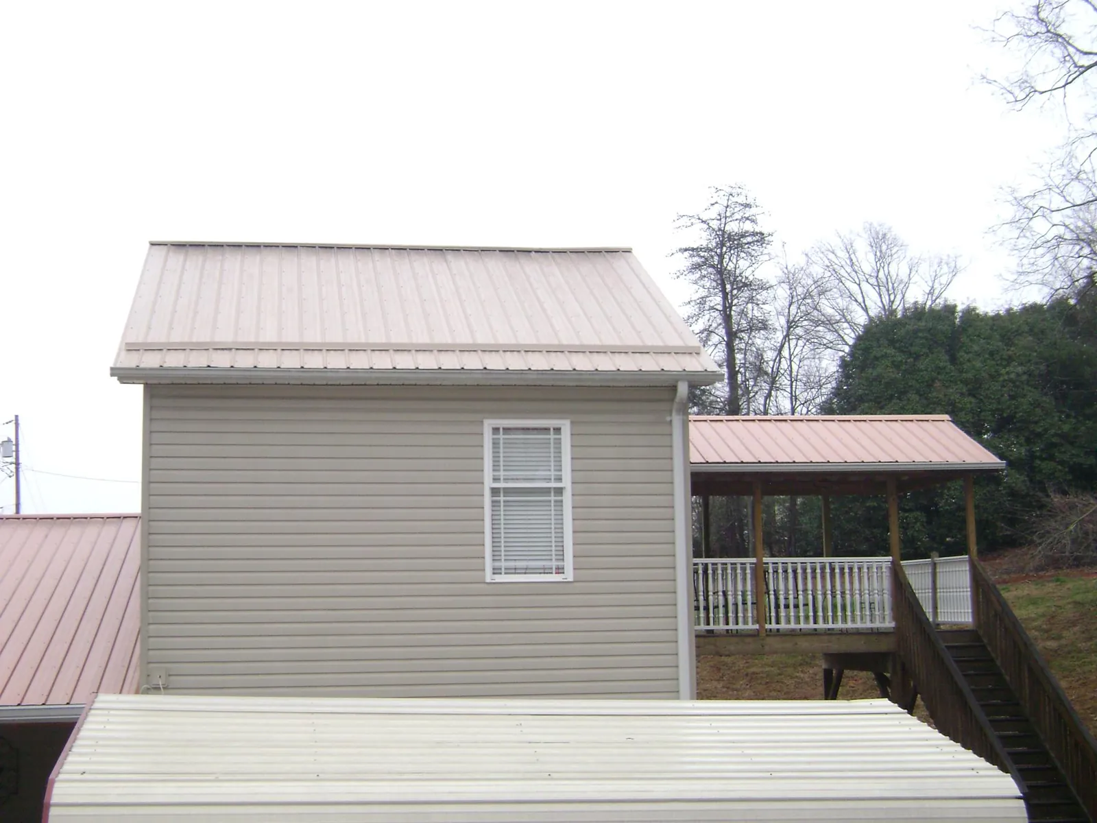 Tan metal roofs on a two story addition and attached porch, from a Roof Replacement job in Kings Mountain